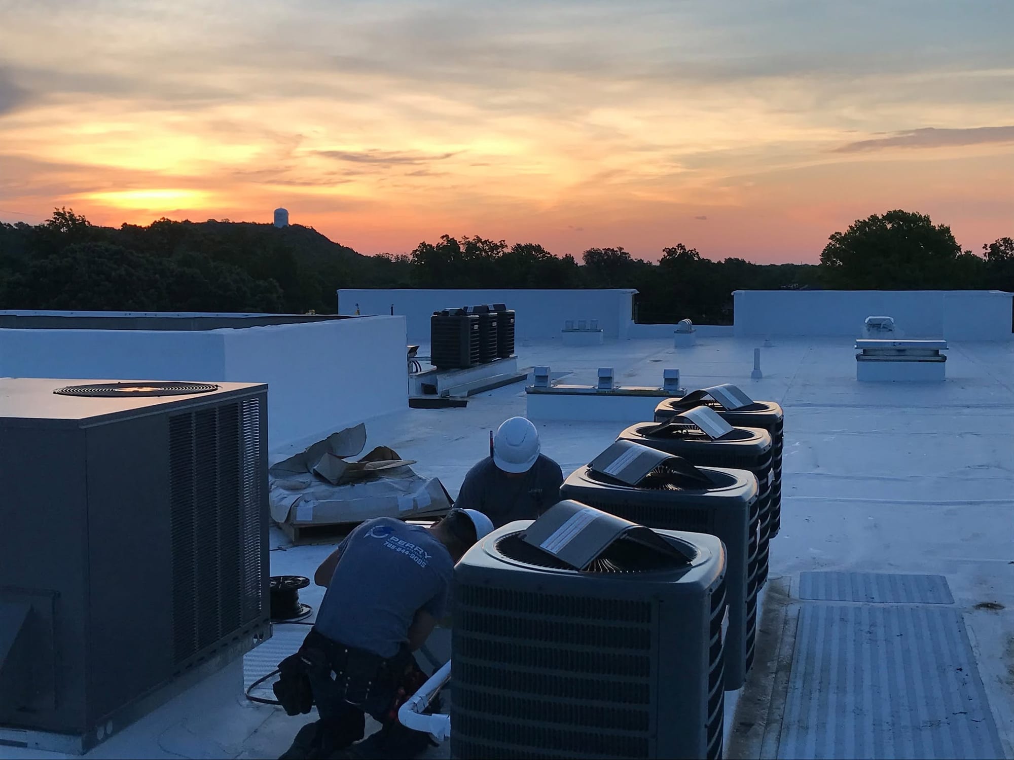 Rooftop mechanical and electrical work on a commercial building at dusk